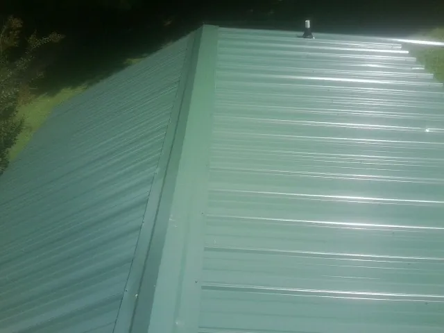 New green metal panels meeting at the ridge of a roof — Flat Roof Repair work by our crew in Walcott