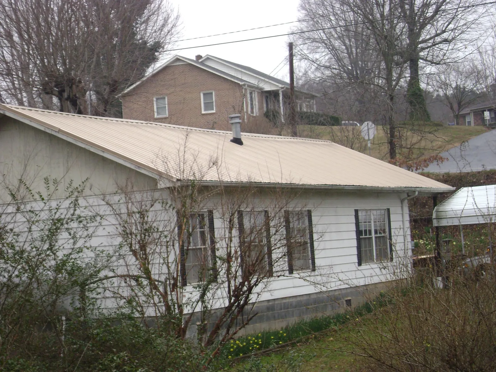 Tan metal roof on a white sided house set into a hillside — Commercial Roofing by Roofing Brothers in Walcott