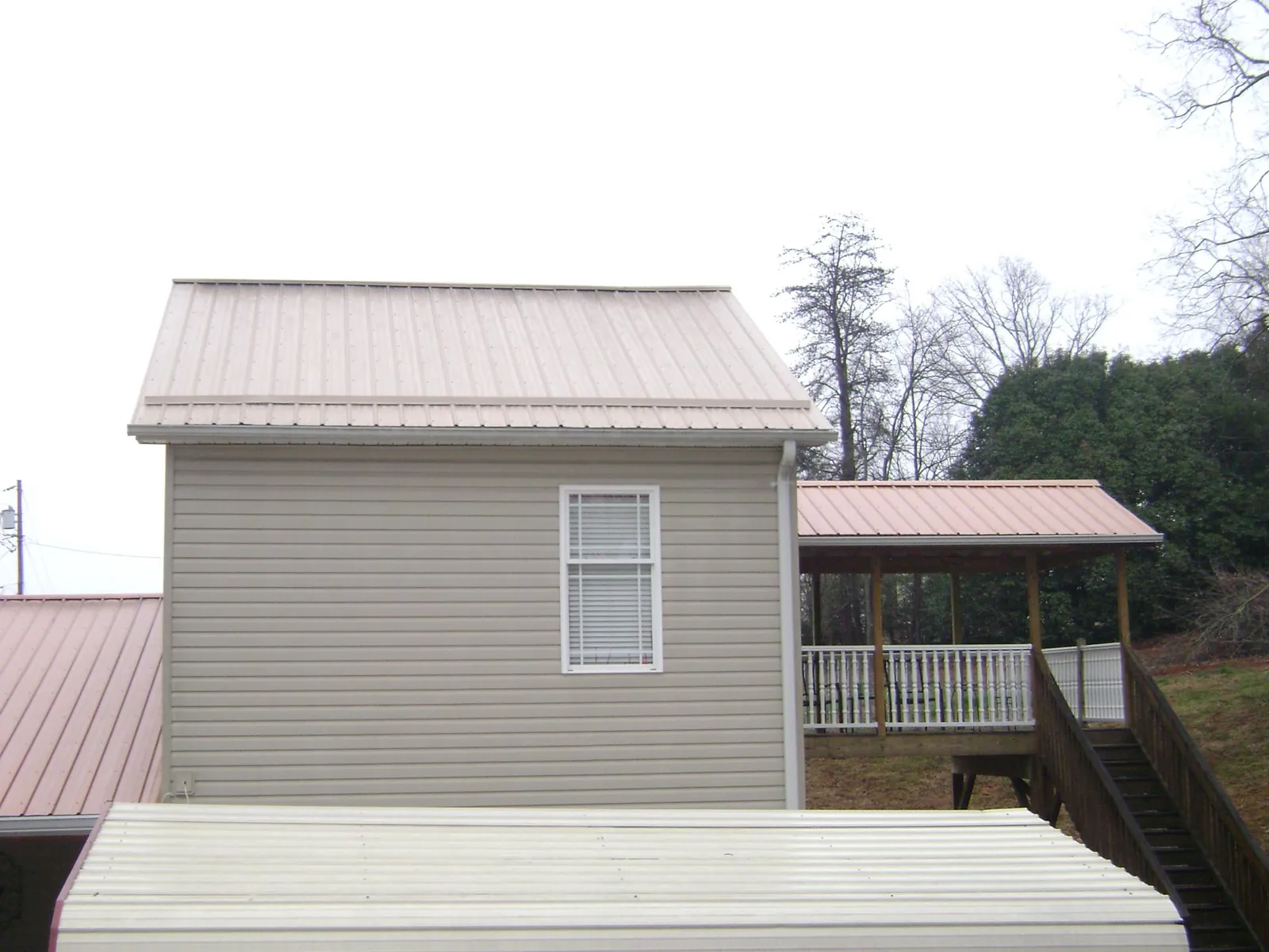 Tan metal roofs on a two story addition and attached porch, from a Roof Replacement job in Walcott